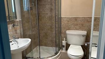 Un baño con ducha envuelta en vidrio, inodoro y lavamanos.