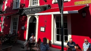 A red building with a sign reading 'CASTLE HOTEL' and outdoor seating. - The Castle Hotel (Aberaeron)