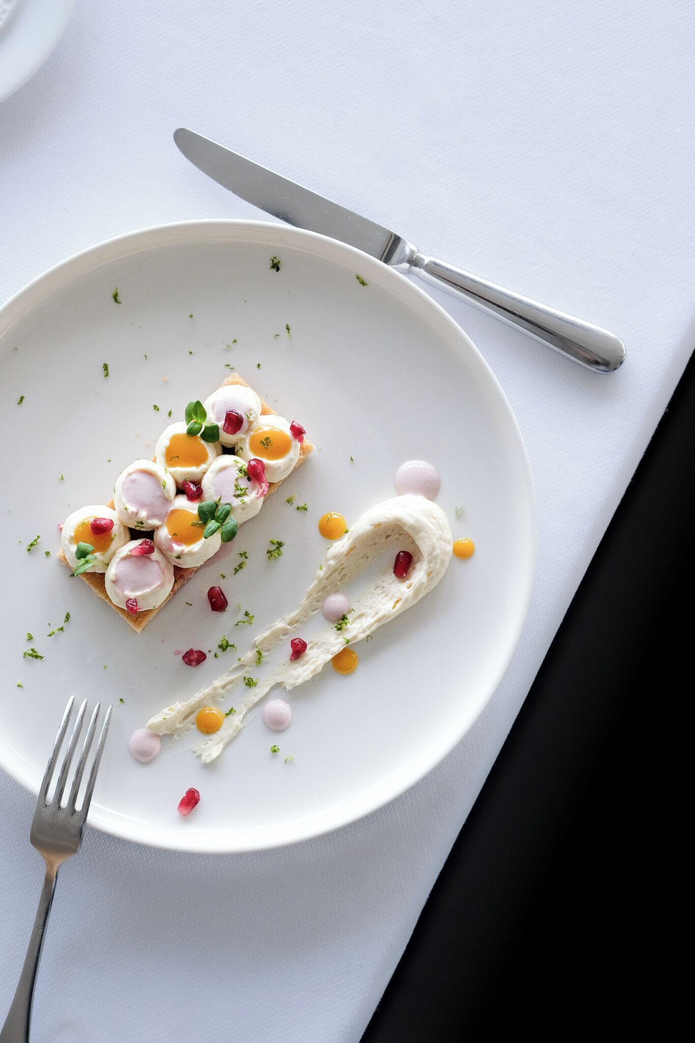 A white plate with a food arrangement, a fork, and a knife on a white tablecloth.