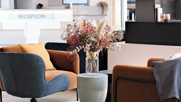 Een receptiegedeelte met een receptiebalie, een vaas met gedroogde bloemen en moderne zitplaatsen.