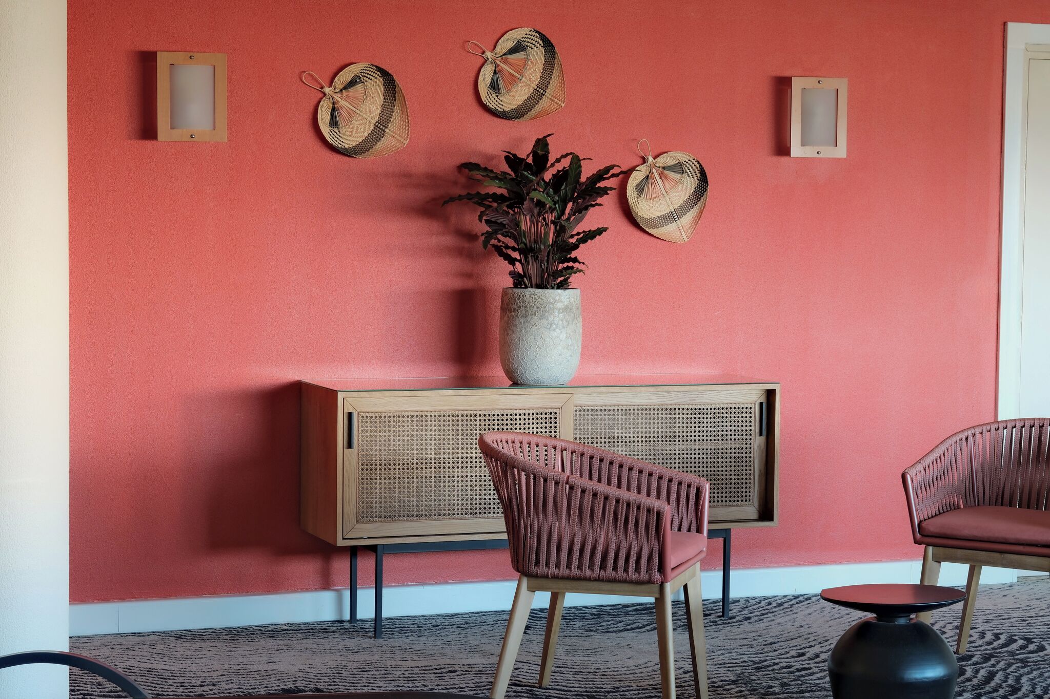 A room with a red wall, a wooden cabinet, a potted plant, and two wicker chairs.