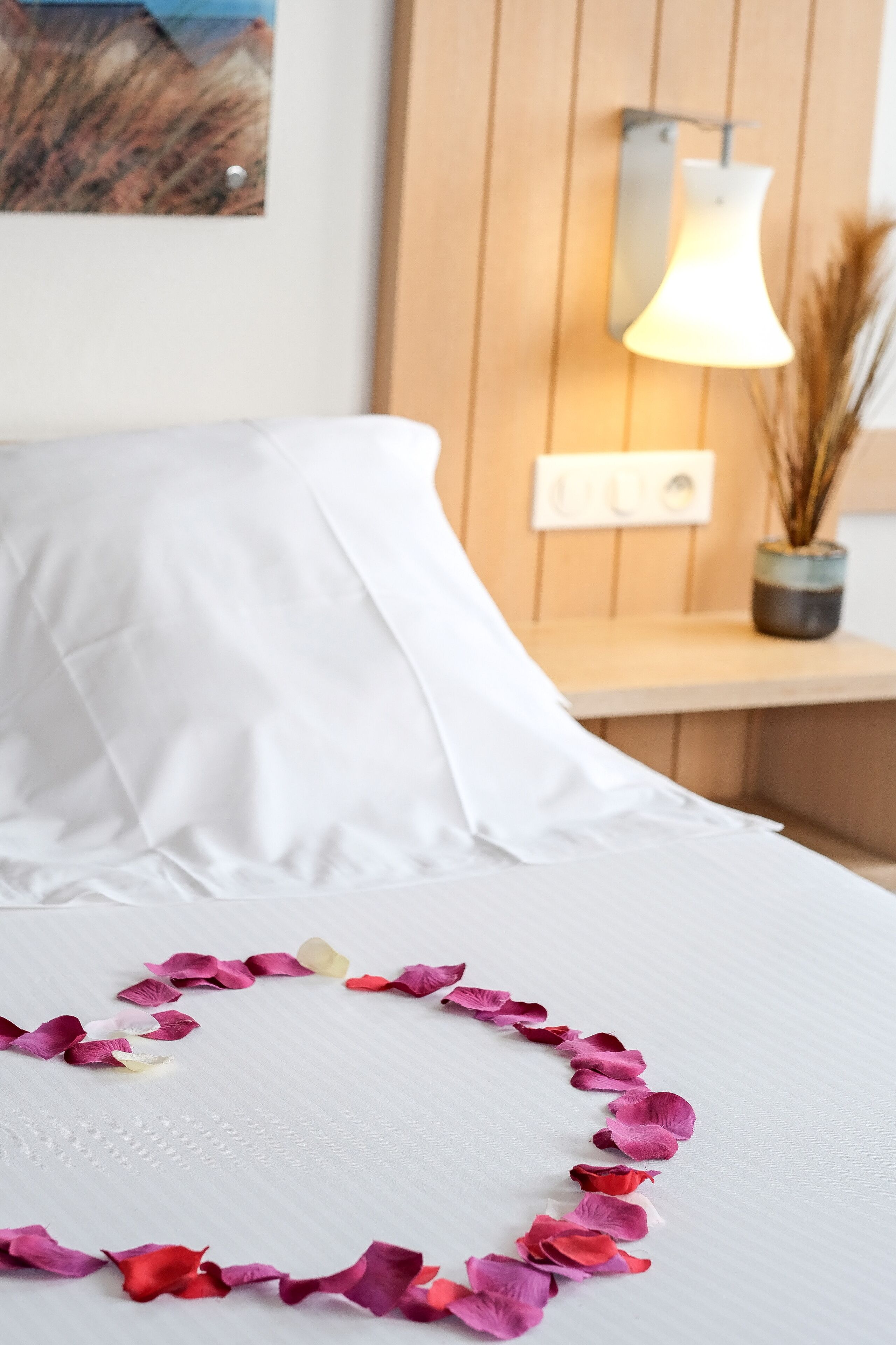 A neatly made bed with white linens and a decorative garland of pink and red flower petals.
