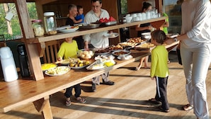 Montaje de bufé con diversos alimentos sobre mesas de madera, rodeado de gente.