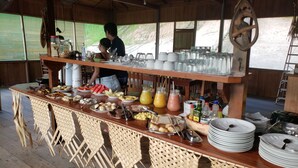 Disposición de bufé con diversas opciones de comida y bebidas, muebles de madera y una persona sirviendo.