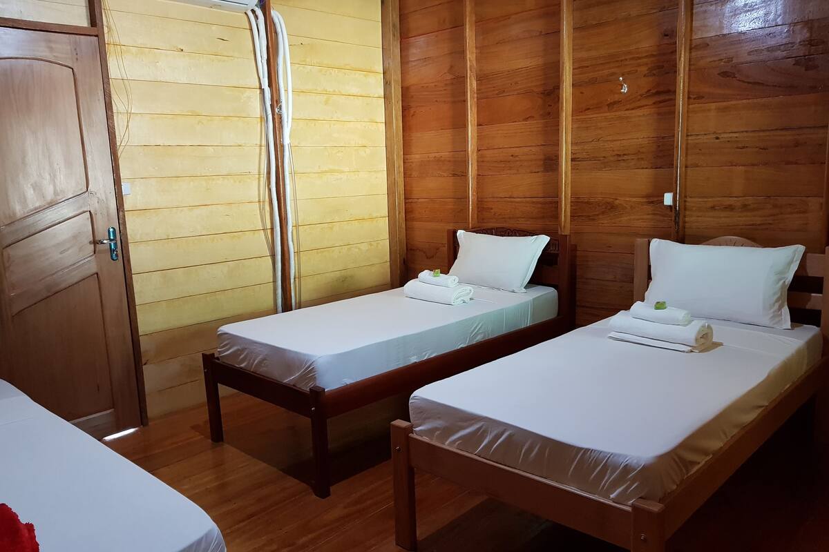 Une chambre avec deux lits en bois, chacun étant équipé de draps et d’oreillers blancs, ainsi qu’une armoire en bois.