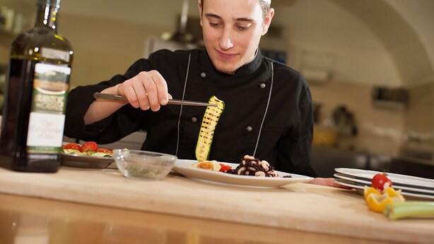 A chef in a professional kitchen setting, preparing food with a focus on a grilled vegetable. - Alle Due Spade (Folgaria)