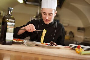 A chef in a professional kitchen setting, preparing food with a focus on a grilled vegetable. - Alle Due Spade (Folgaria)
