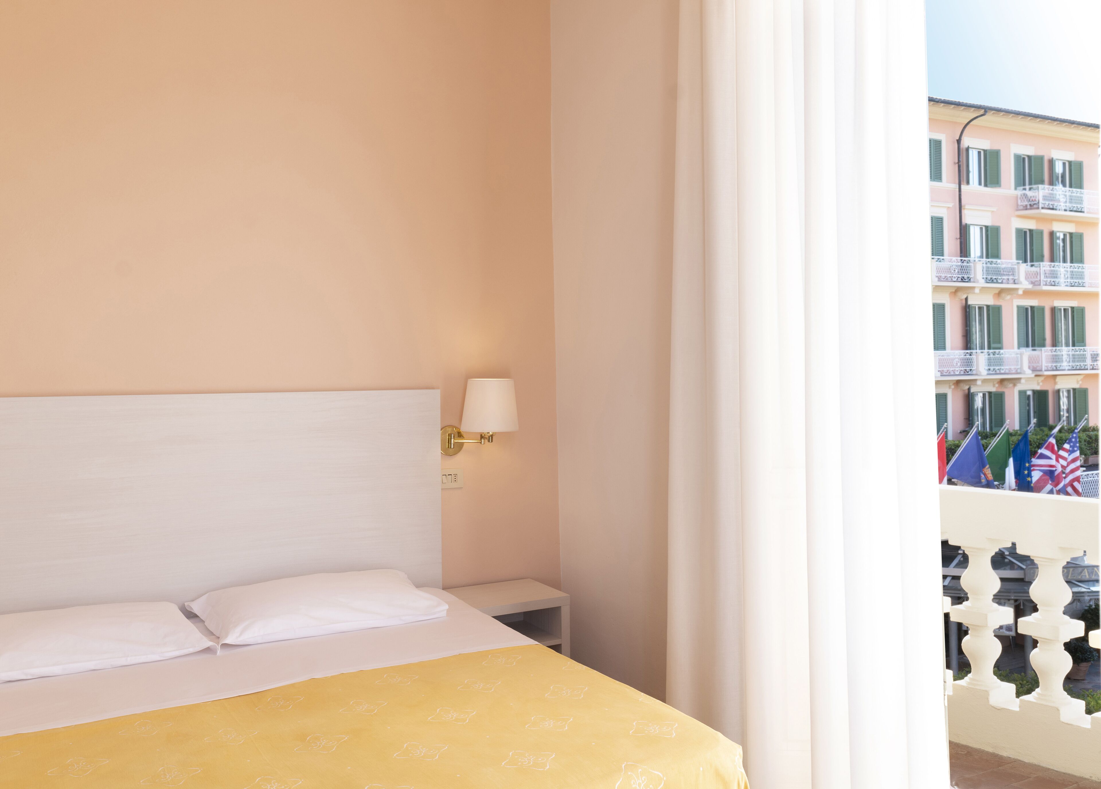 A hotel room with a bed, a nightstand, a lamp, and a view of the city through a balcony.
