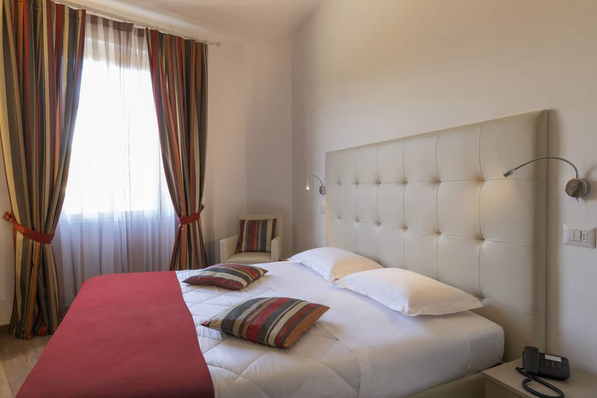 Une chambre d’hôtel avec un grand lit, une table de chevet avec un téléphone, une chaise et une fenêtre avec des rideaux.