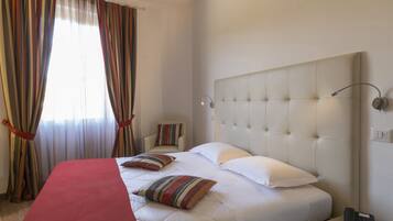 A hotel room with a large bed, a bedside table with a phone, a chair, and a window with curtains.