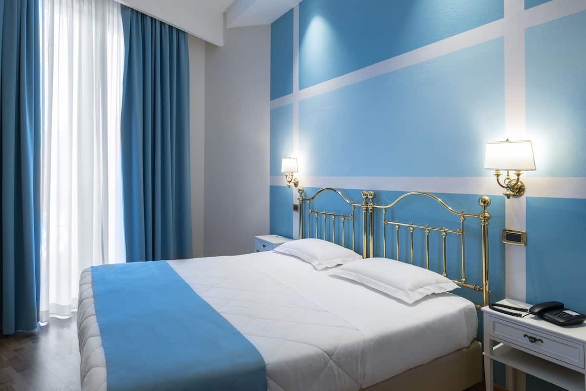 Un lit bien fait, avec une couvre-lit blanche et bleue, une tête de lit dorée et deux lampes de chevet.