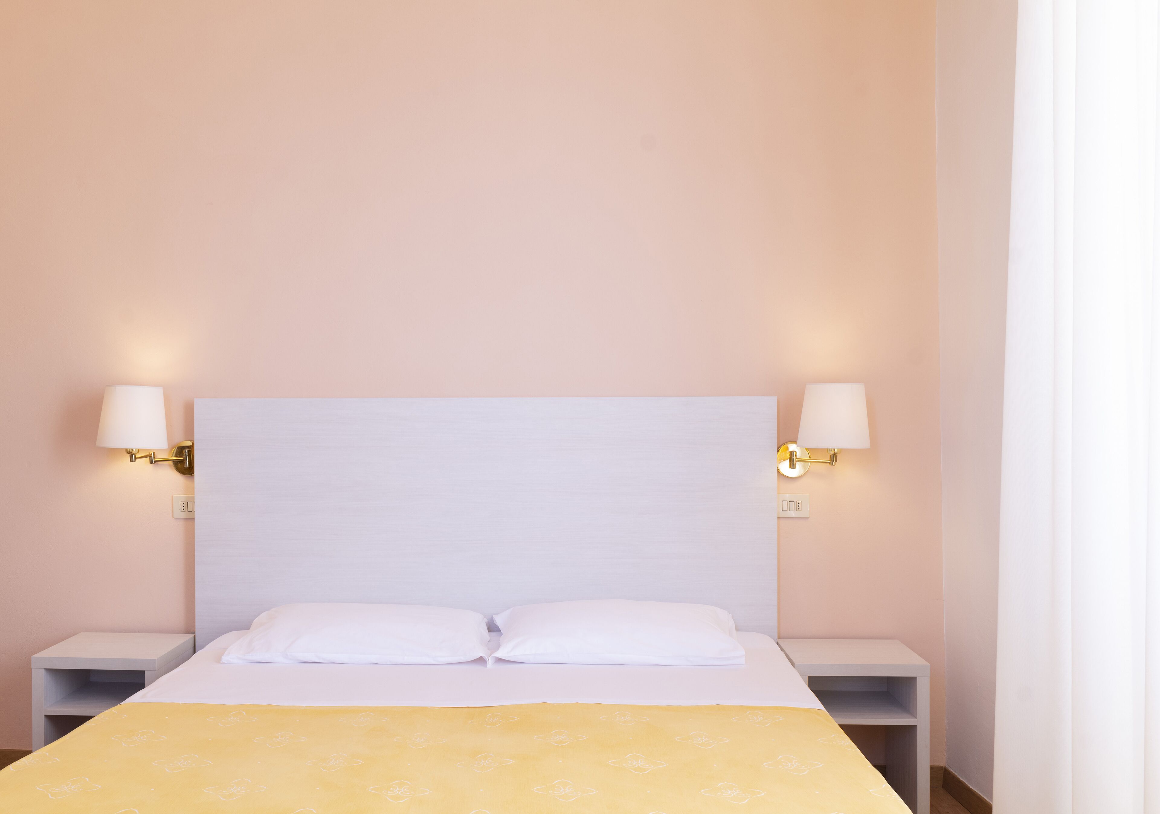 A hotel room with a large bed, two bedside tables, and wall-mounted lamps.