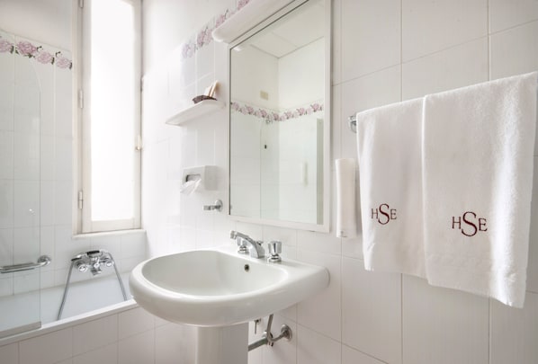 Un baño con un lavamanos blanco, un espejo y dos toallas con el bordado "HSE".