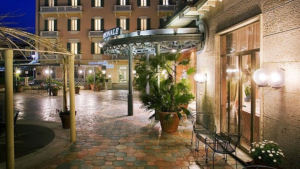 A hotel courtyard with a covered walkway, potted plants, and outdoor seating. - Settentrionale Esplanade (Montecatini Terme)