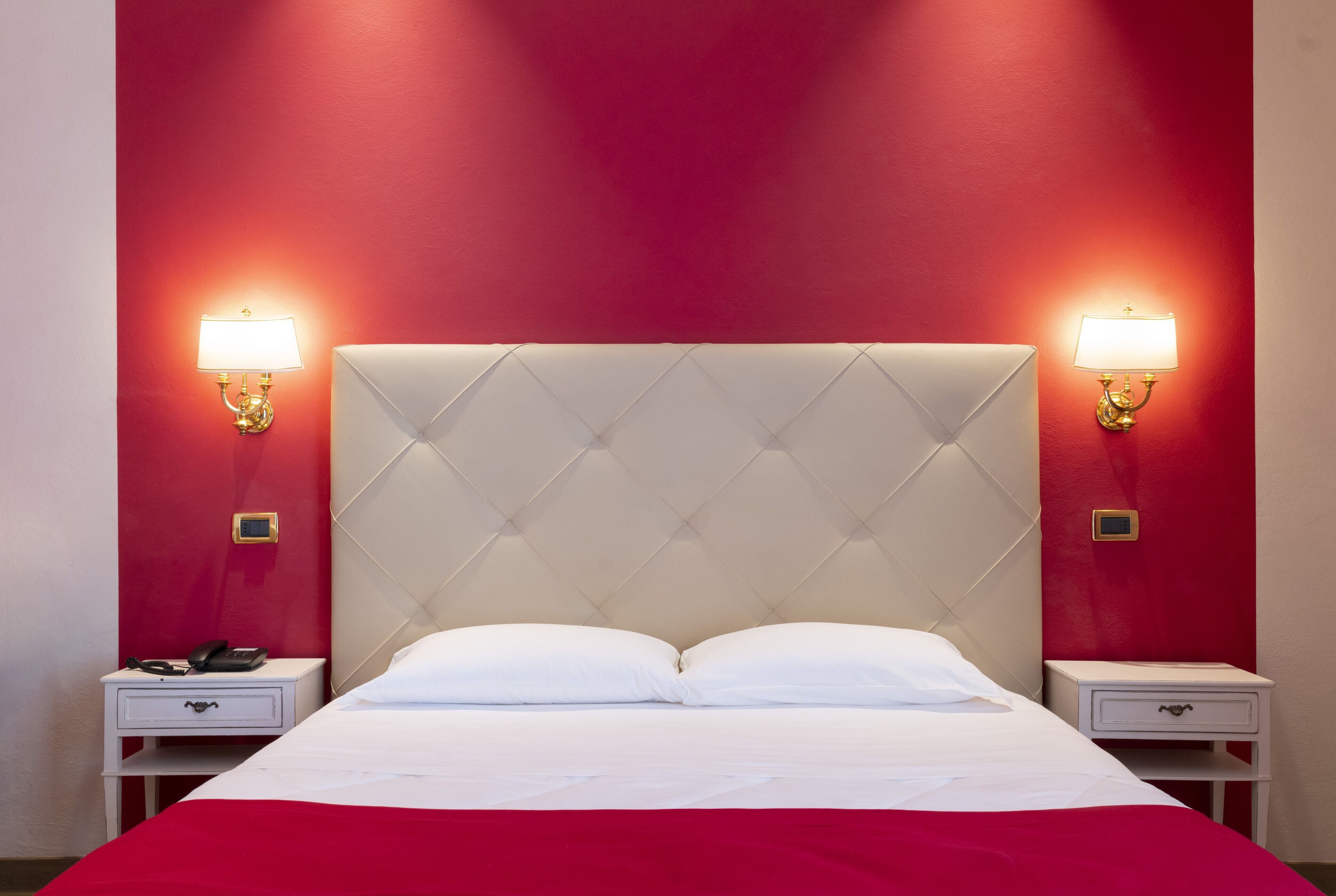 A hotel room with a large bed, two bedside tables, and two wall-mounted lamps.