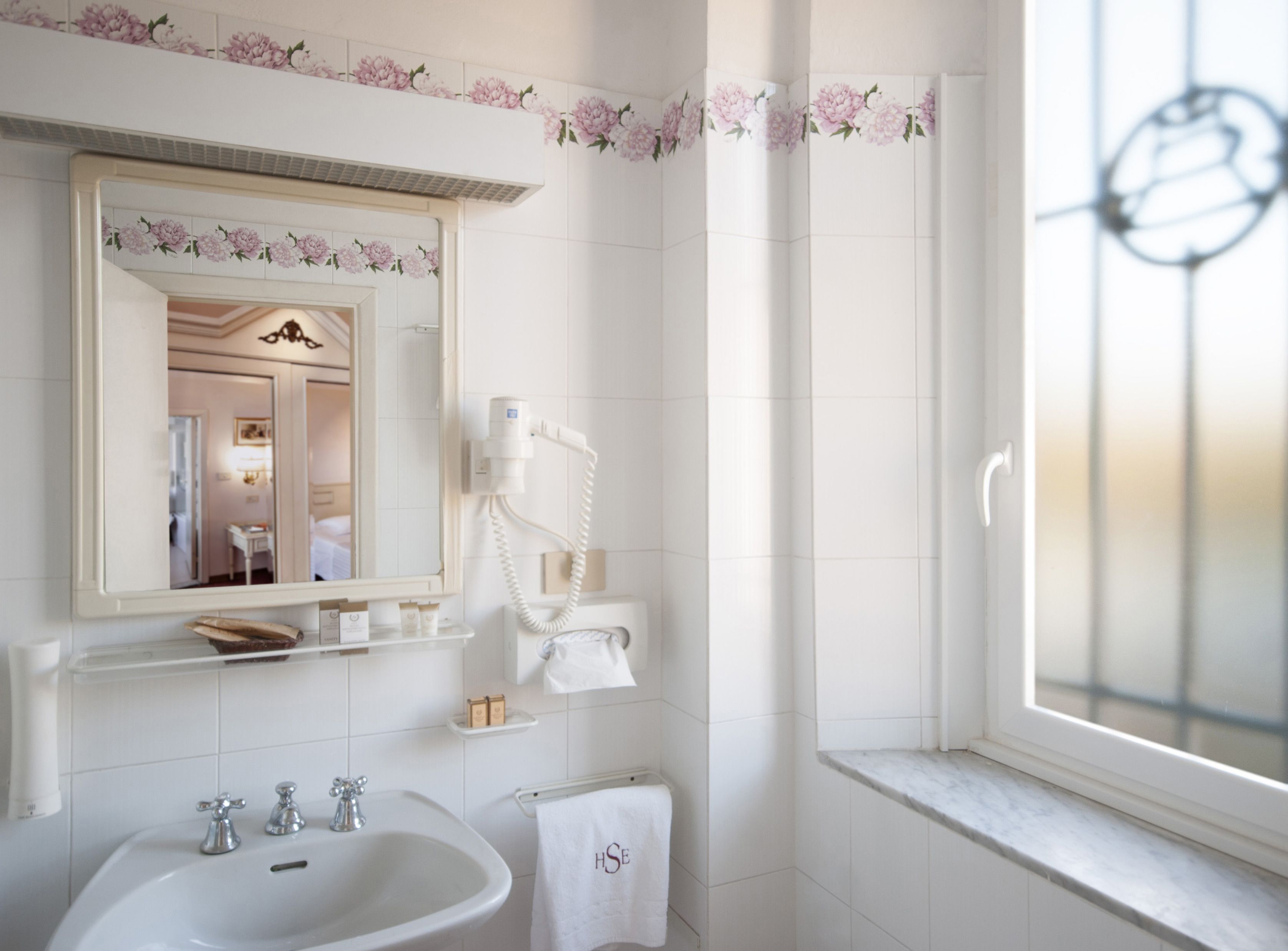 A bathroom with a large mirror, a hairdryer, a sink, and a window with a view.
