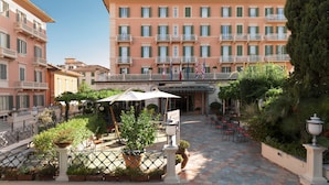 A hotel courtyard with outdoor seating, potted plants, and a large building with balconies. - Settentrionale Esplanade (Montecatini Terme)