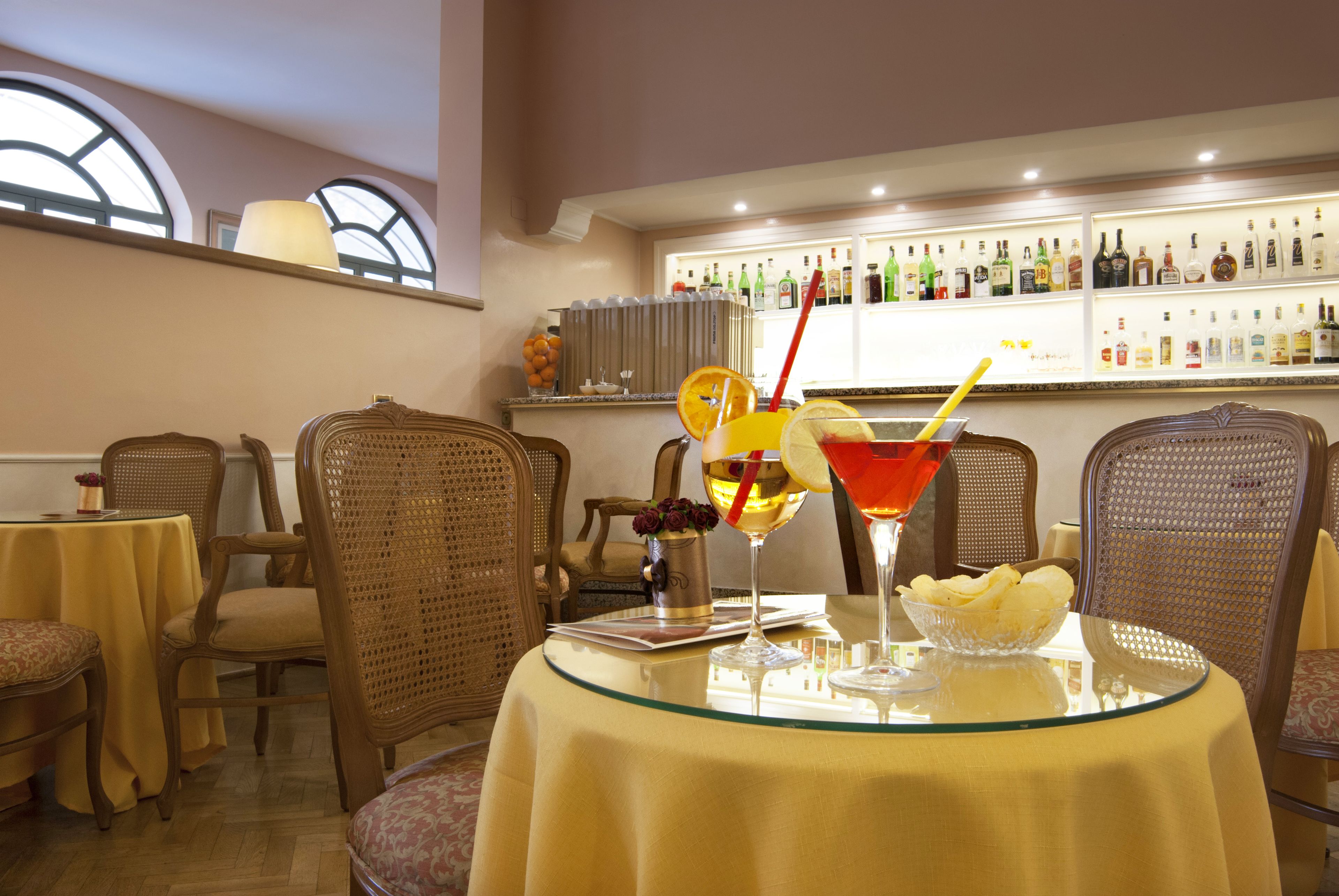 A dining area with wicker chairs, a glass table, and a bar with bottles in the background.