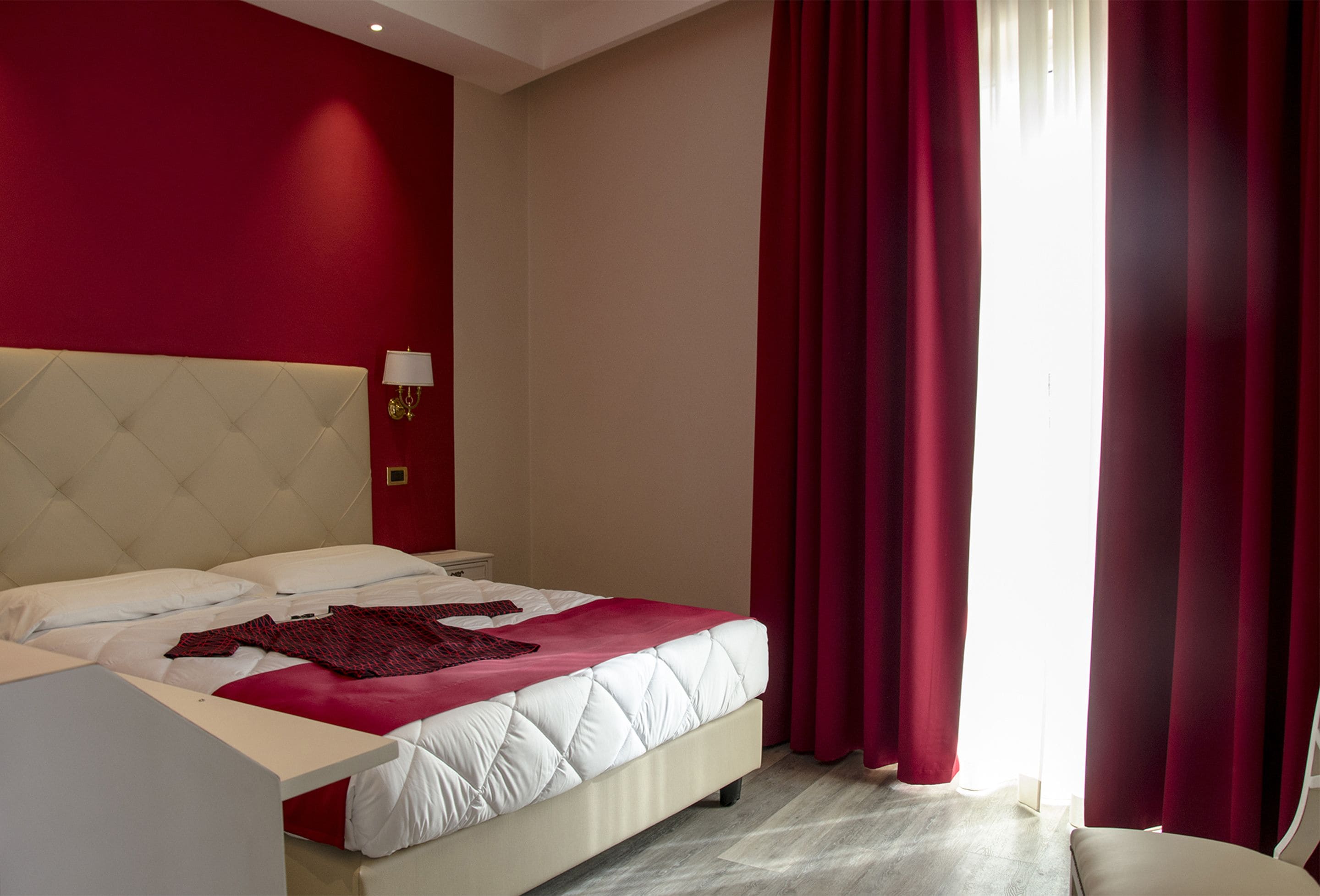 Una habitación de hotel con una cama grande, cortinas rojas y un cabecero blanco.