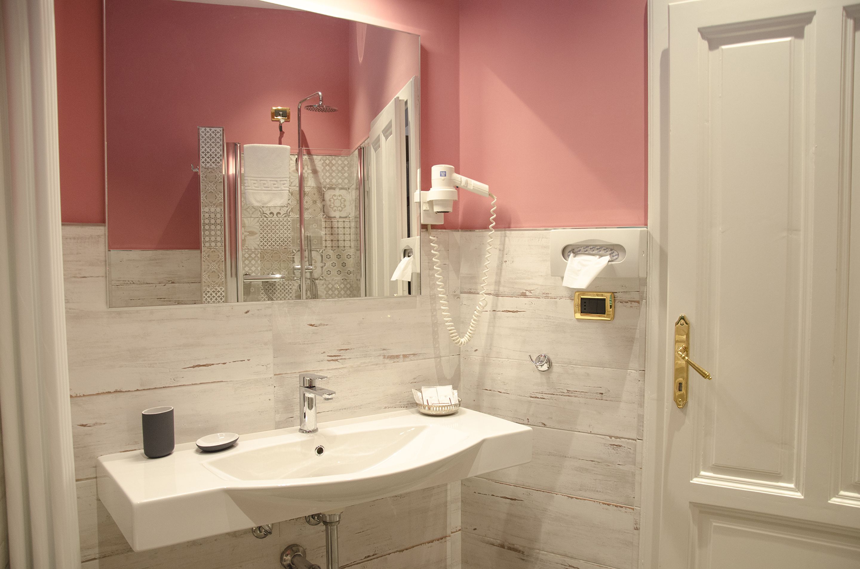 A bathroom with a white sink, a mirror, a shower, and a door with a gold handle.