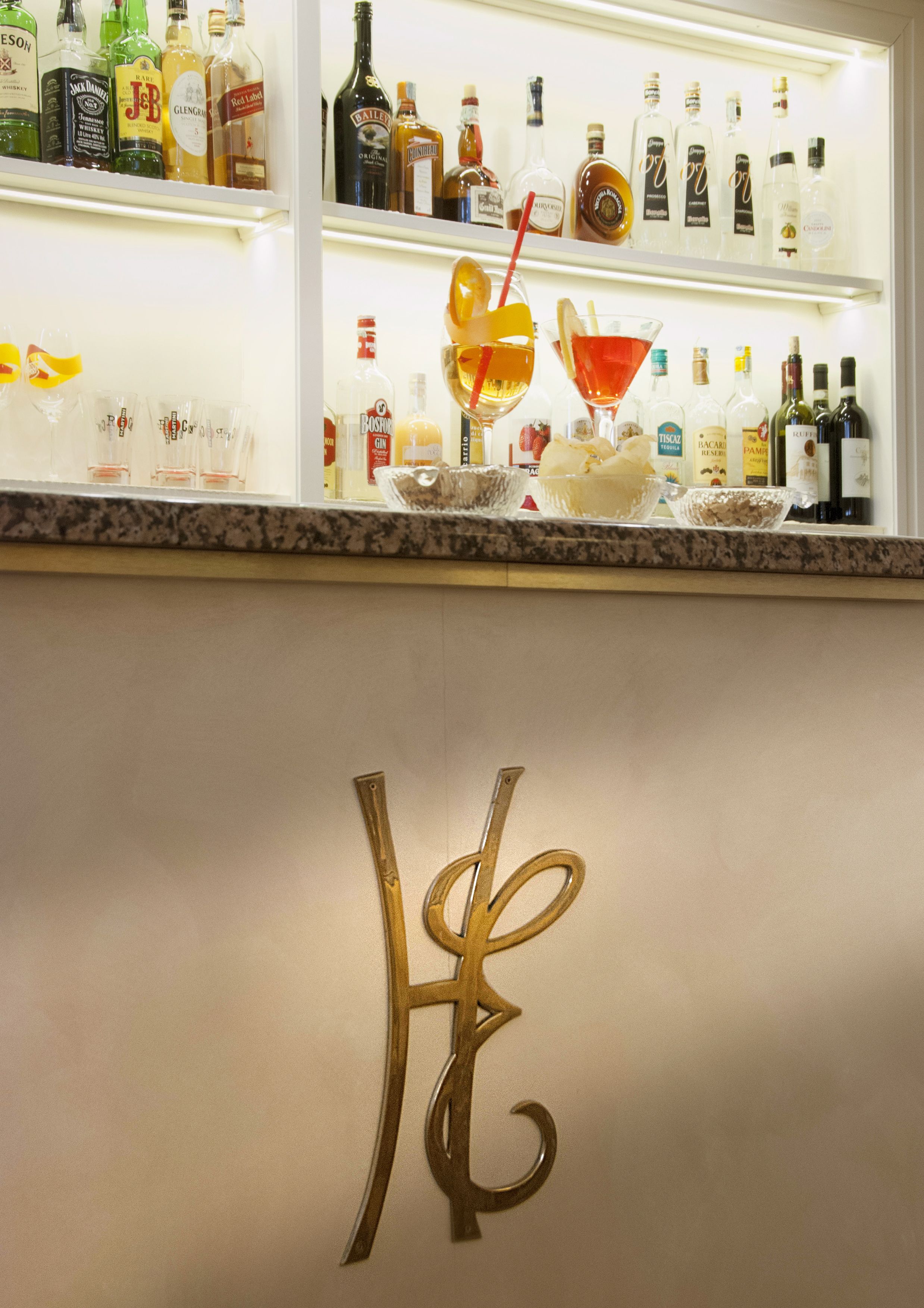 A bar area with shelves of liquor bottles and a decorative letter 'H' on the wall.
