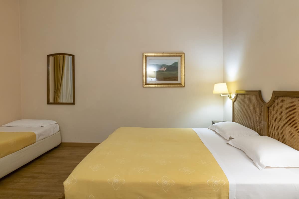 Une chambre d’hôtel avec deux lits simples, un grand lit, un tableau au mur et une lampe de chevet.