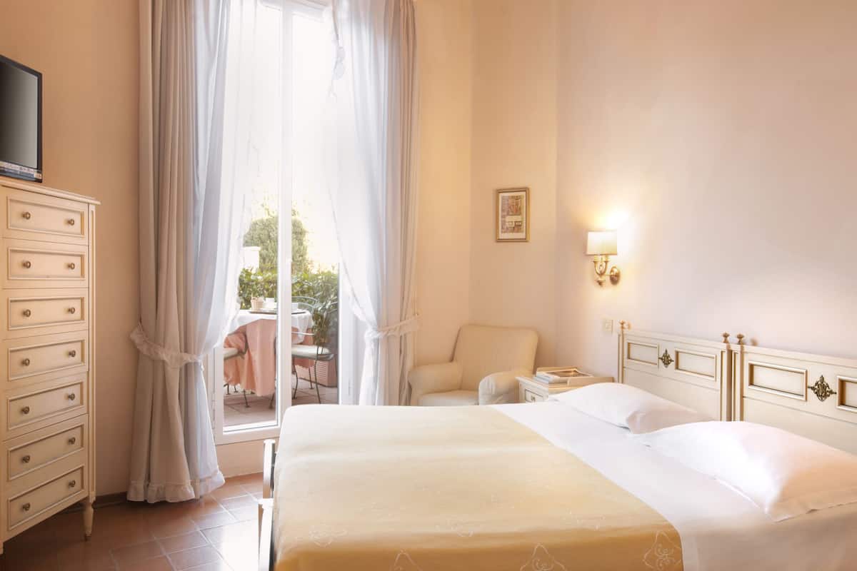 Une chambre d’hôtel équipée d’un lit, d’une télévision, d’une commode, d’une chaise et d’une table, avec vue sur l’extérieur.