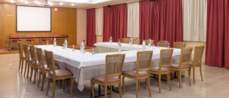 A conference room with a long table, chairs, a projector screen, and curtains.