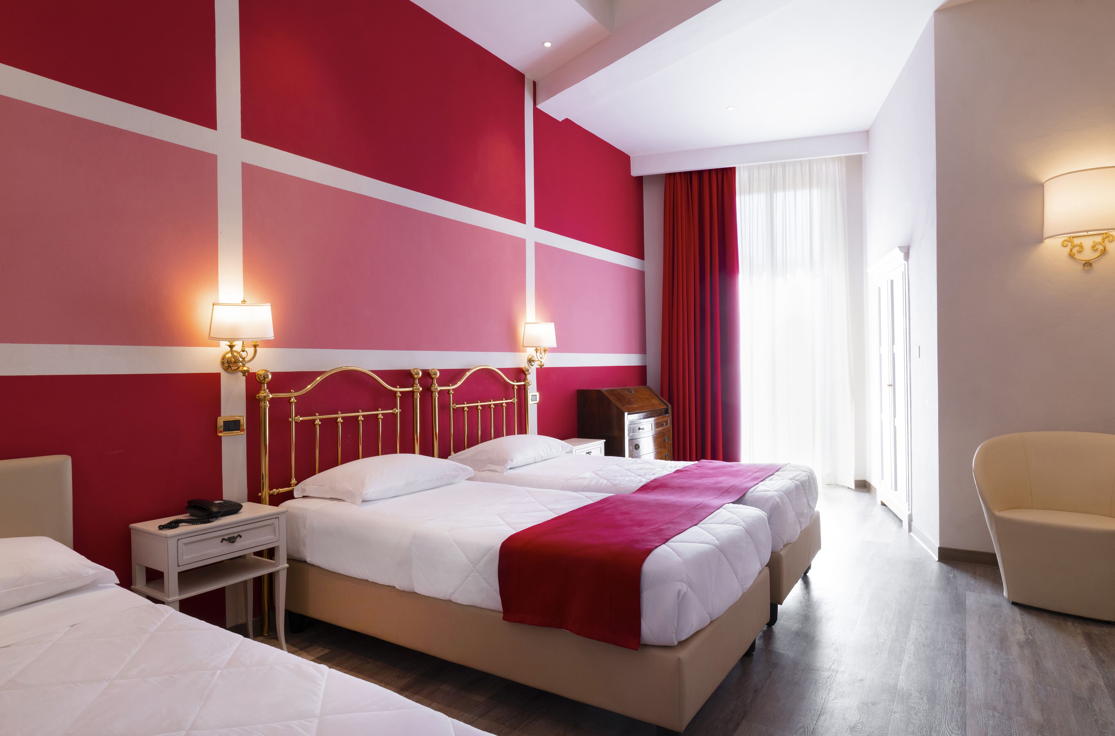 Una habitación de hotel con una cama grande, dos mesitas de noche, una silla y un ventanal con cortinas.