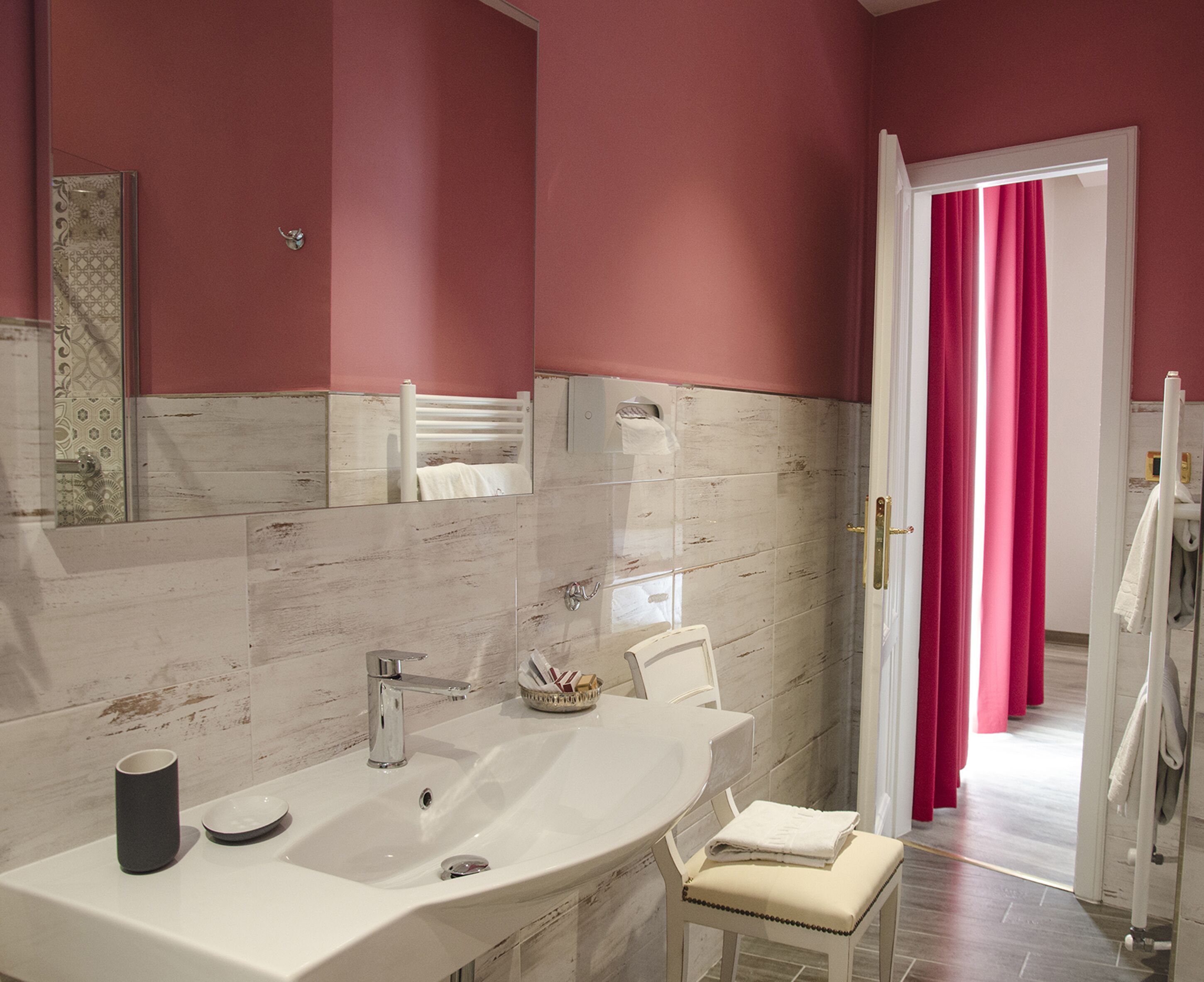 A bathroom with a large mirror, a sink, a chair, and a shower area.
