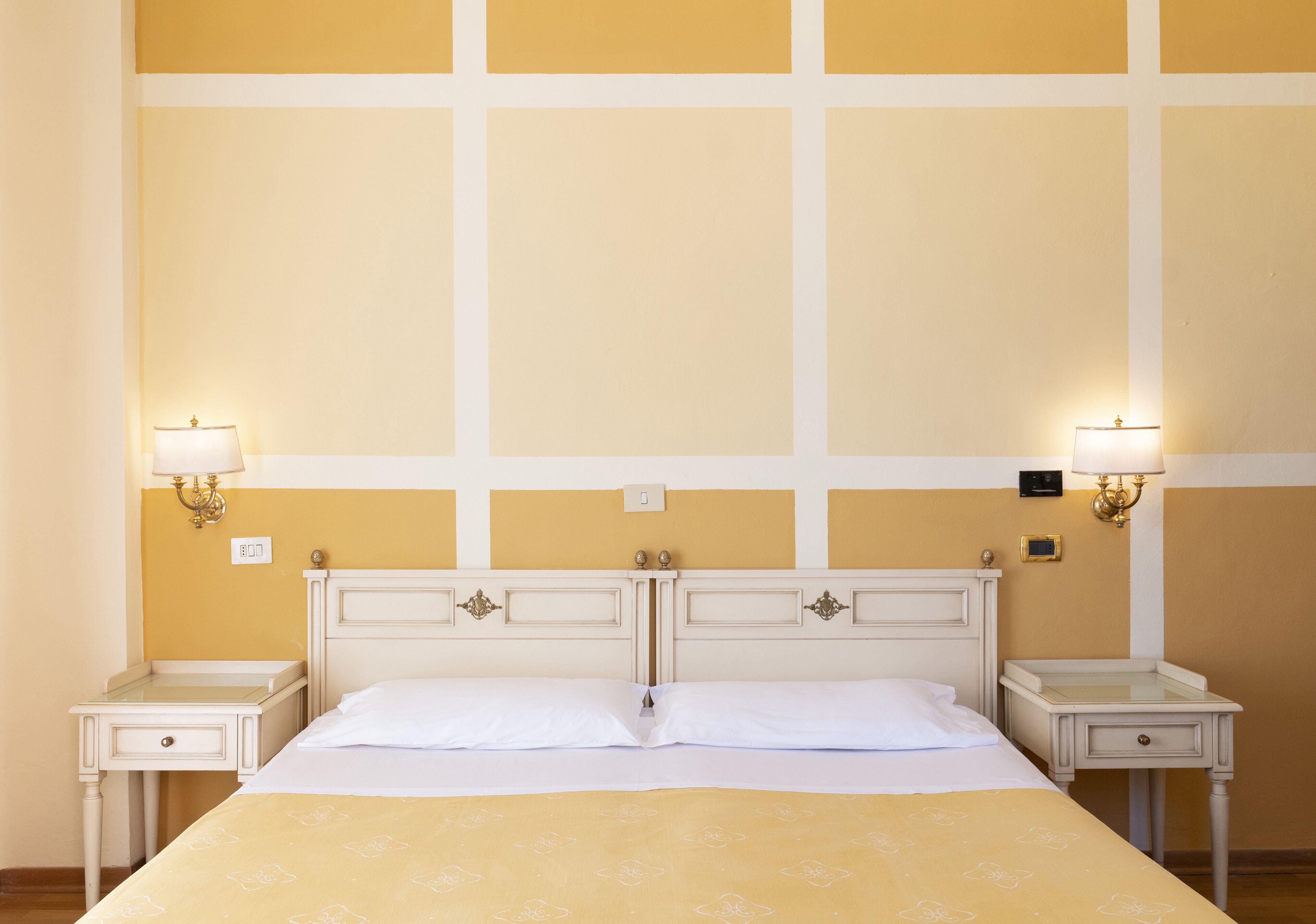 A hotel room with a bed, two bedside tables, and wall-mounted lamps.