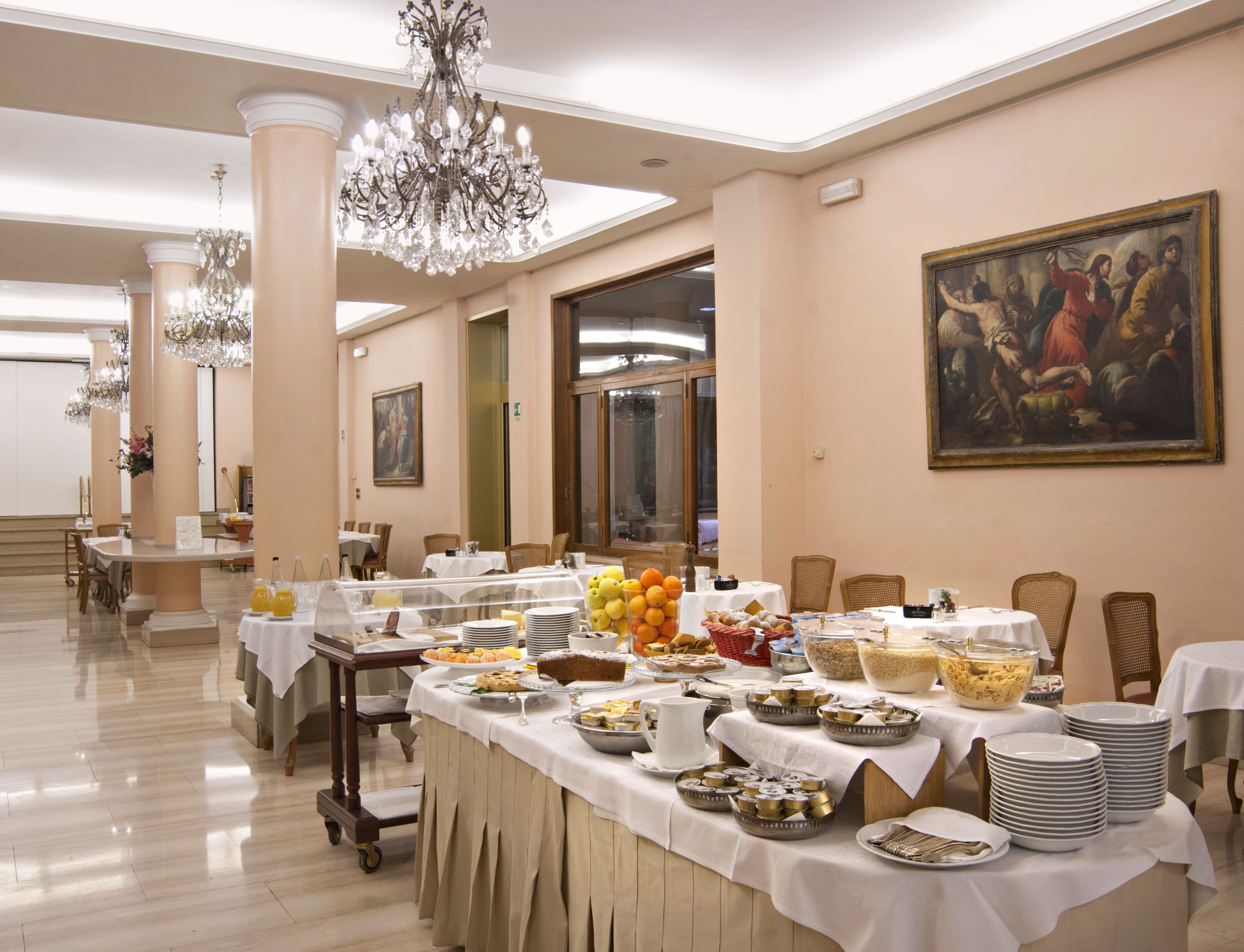 A banquet hall with tables set for a meal, a chandelier, and a painting on the wall.