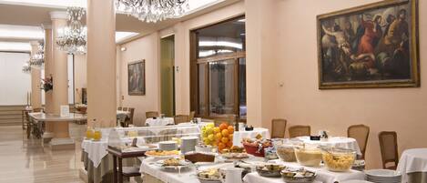 A banquet hall with tables set for a meal, a chandelier, and a painting on the wall.