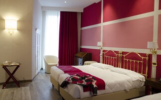 Habitación de hotel con una cama grande, una silla, una mesita con una bandeja de objetos y una ventana con cortinas.