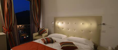 A hotel room with a large bed, a nightstand, a chair, and a window with curtains.