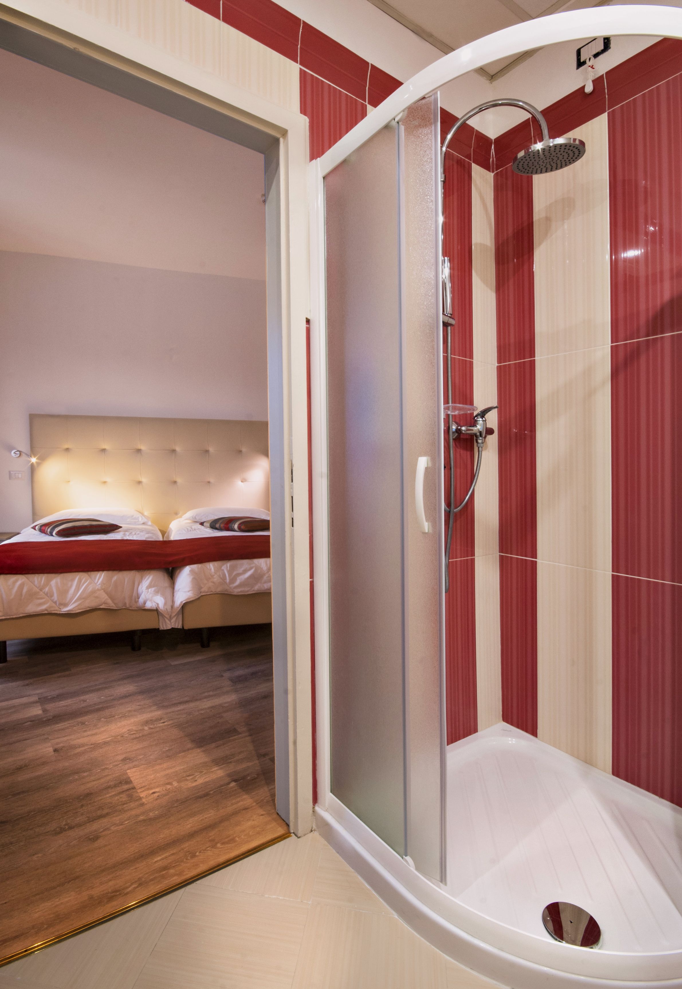 Une chambre d’hôtel dotée d’une douche en verre, d’un lit avec une literie rouge et d’un plancher en bois.