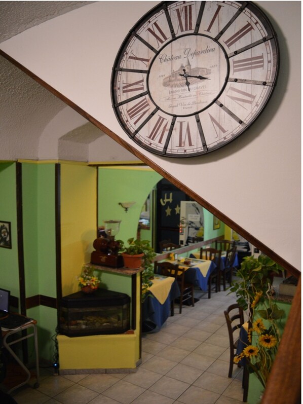 A dining area with a large wall clock, green walls, and a table with a blue tablecloth.
