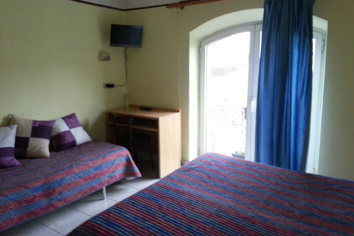 A room with two beds, a desk, a television, and a window with curtains.