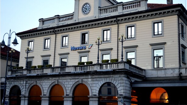 A hotel with a clock tower, arched windows, and a balcony with plants.