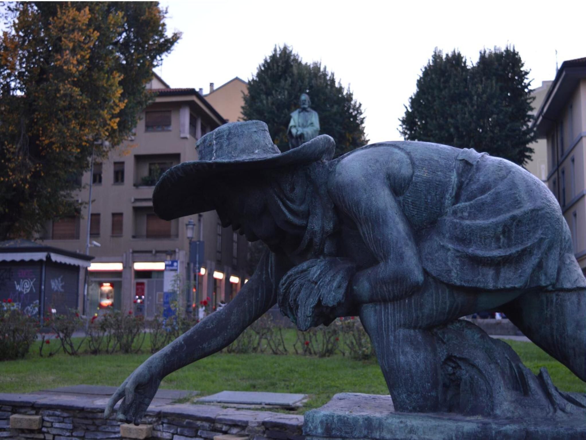 Eine Statue eines Mannes mit Hut, der sich über eine Steinmauer beugt.