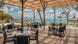 An outdoor dining area with tables and chairs, a wooden deck, and a view of the ocean. - Crystals Beach Resort Belle Mare, a member of Radisson Individuals (Belle Mare)