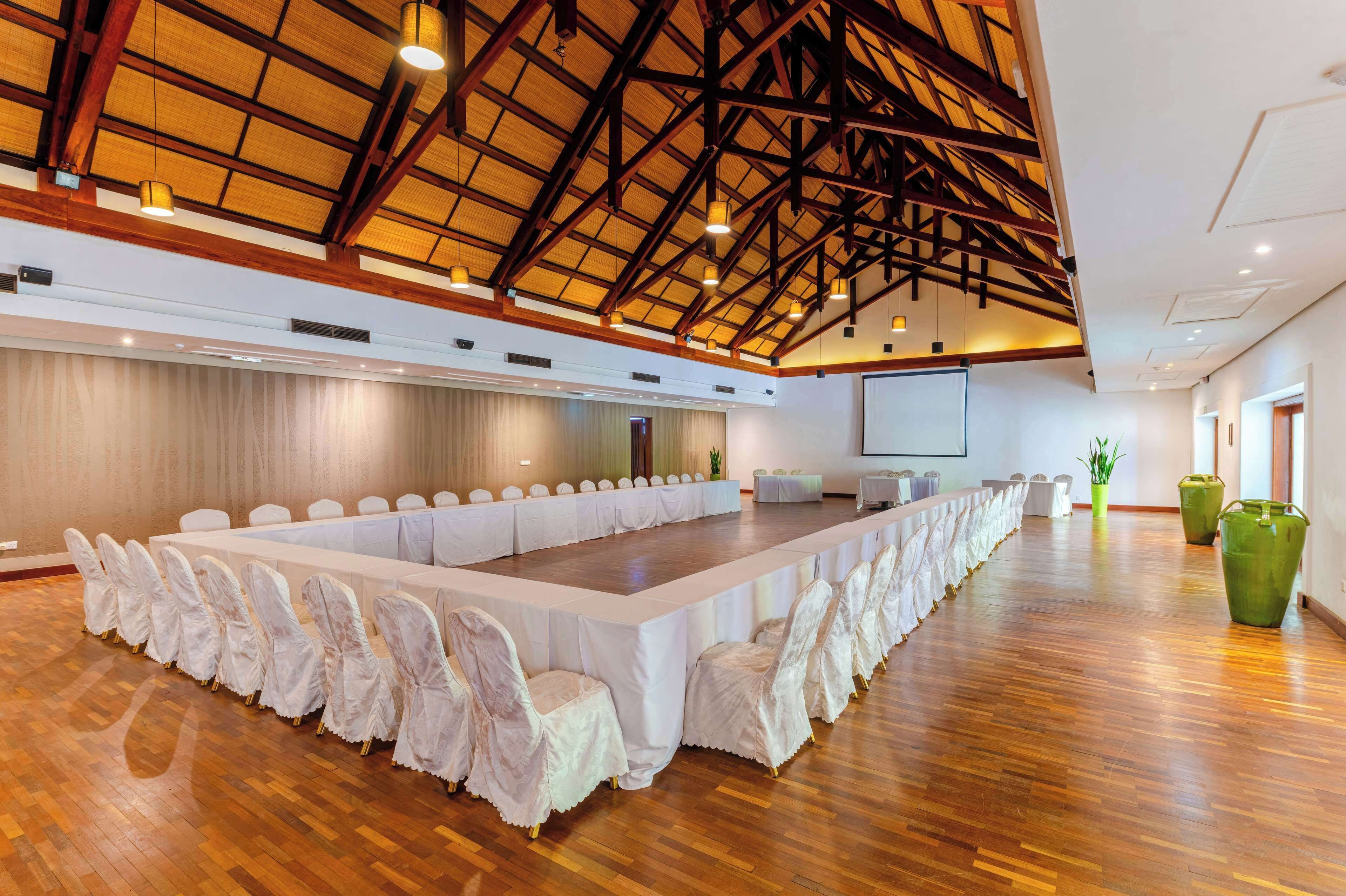A conference room with a long table and chairs, wooden floors, and a high ceiling with exposed beams.