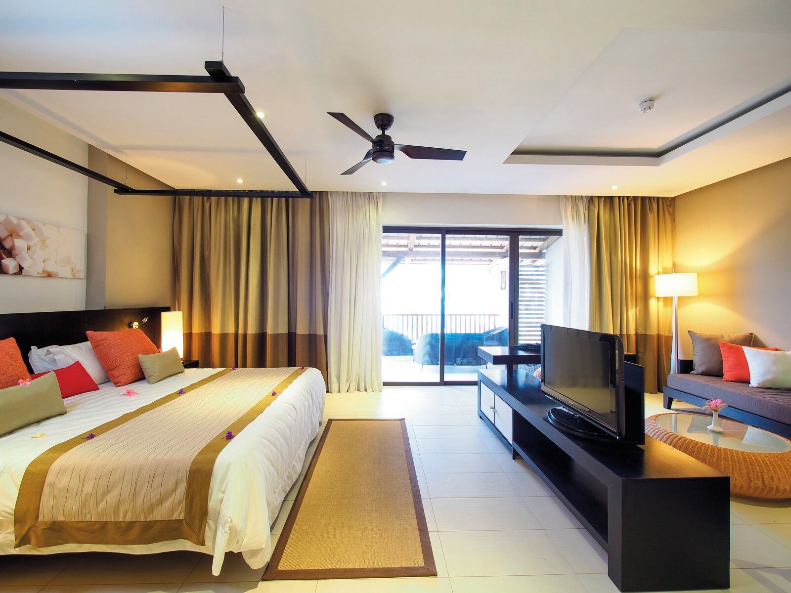 Habitación de hotel con cama, televisión, sofá, balcón y ventilador de techo.