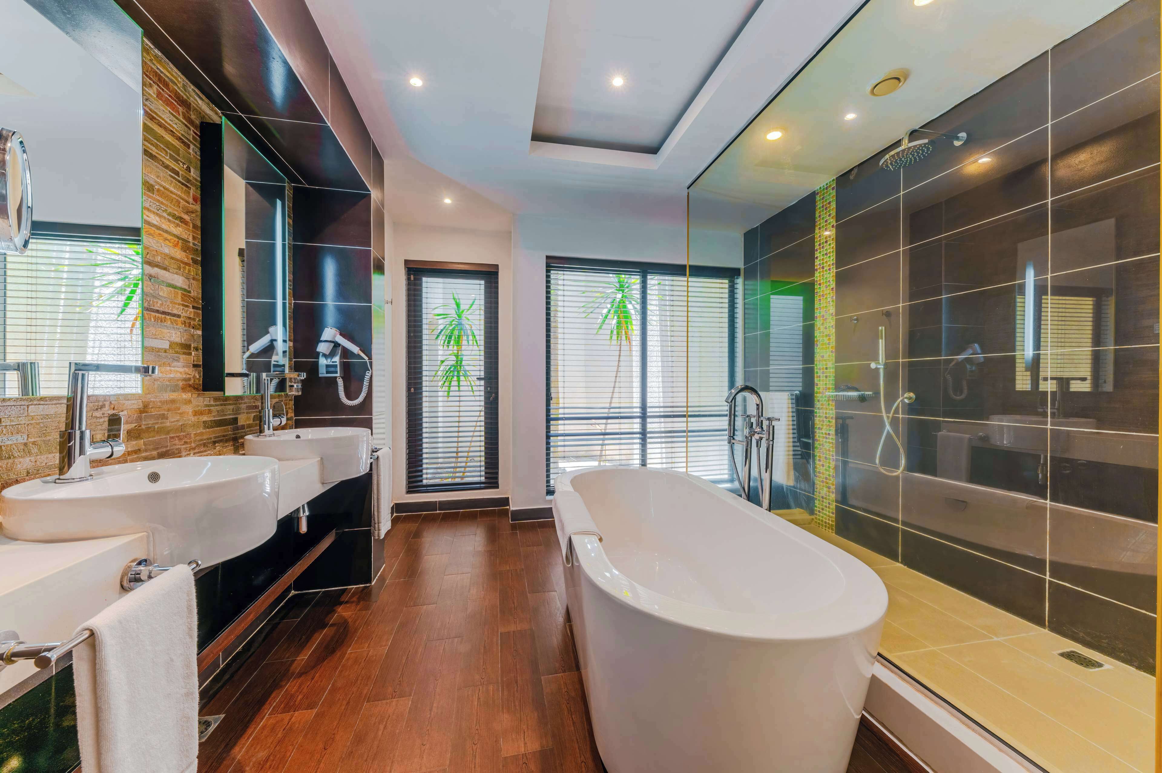 Uma casa de banho moderna com duas lavatórios, uma banheira e zona de duche com divisória de vidro.
