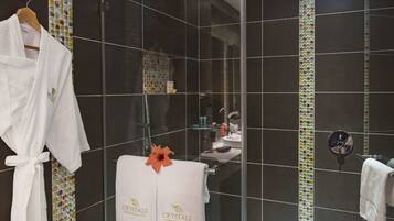 Un baño con baldosas oscuras, mampara de ducha de vidrio, bata blanca y toalla con la marca 'CRYSTALS Wellness & Beauty Care'.
