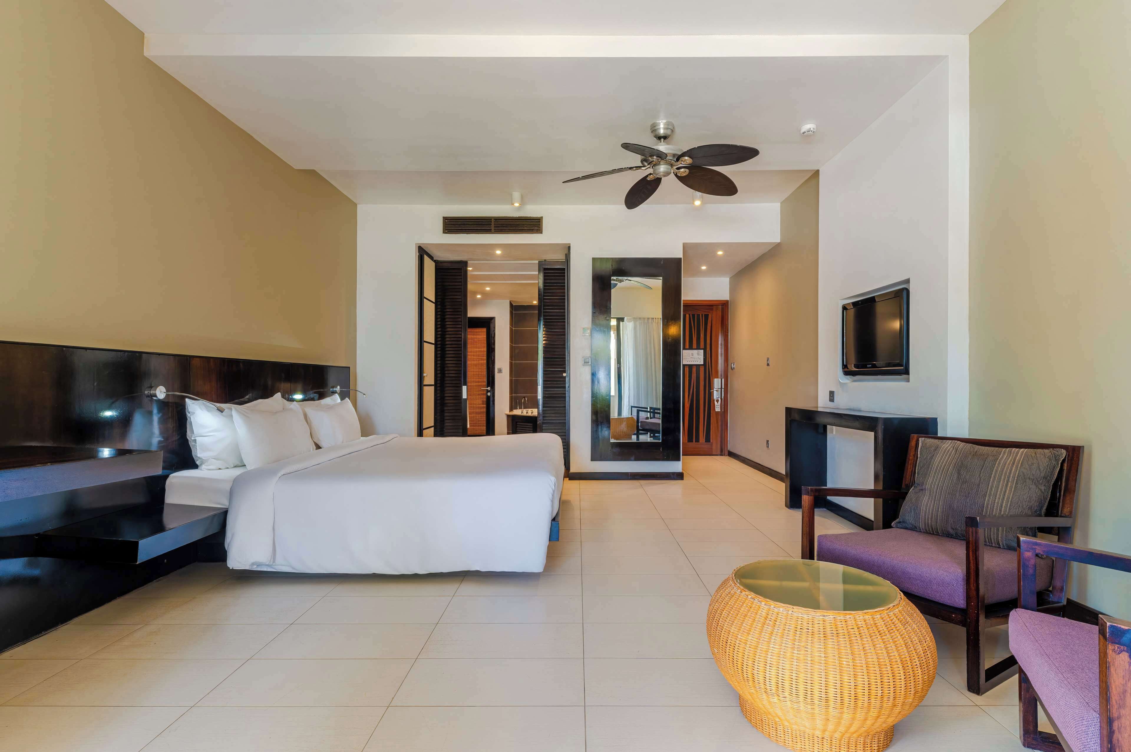 Una habitación de hotel moderna con una cama grande, un sofá, un televisor y un ventilador de techo.