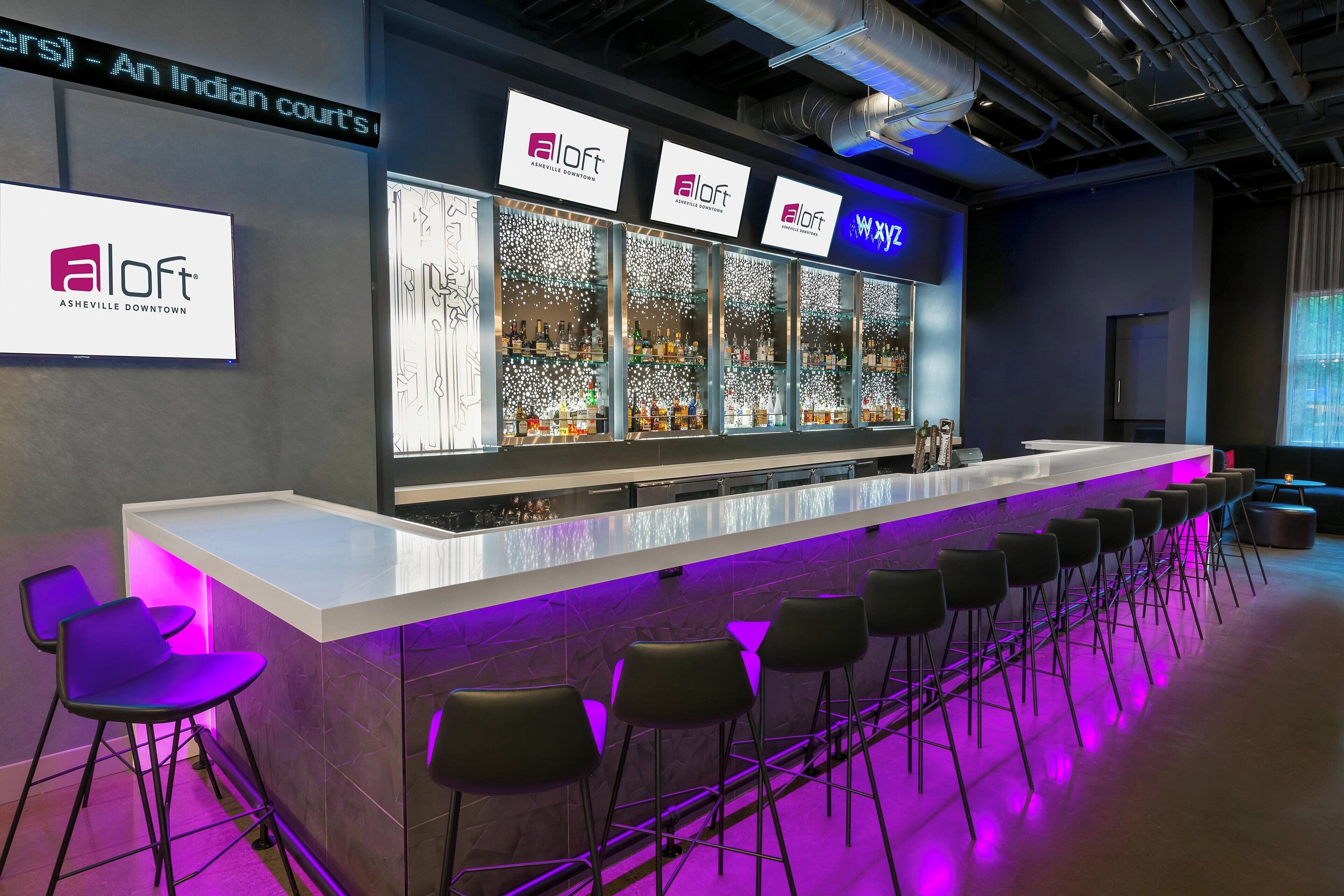 A bar area with multiple seating options, a counter with a neon sign, and a large illuminated display.