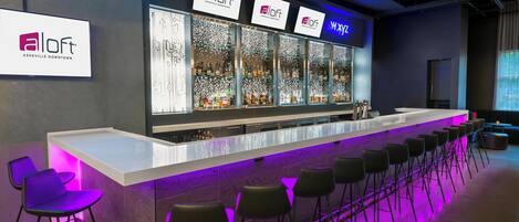 A bar area with multiple seating options, a counter with a neon sign, and a large illuminated display.