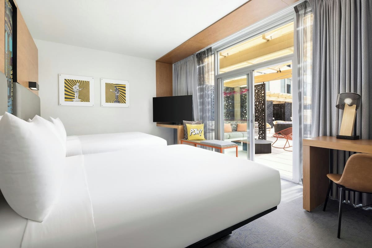 A modern hotel room with a large bed, a desk, a chair, a TV, and a view of the outdoor area.