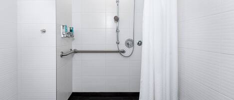 A modern bathroom with white tiled walls, a black floor, a shower with a handheld showerhead, a grab bar, and a white curtain.